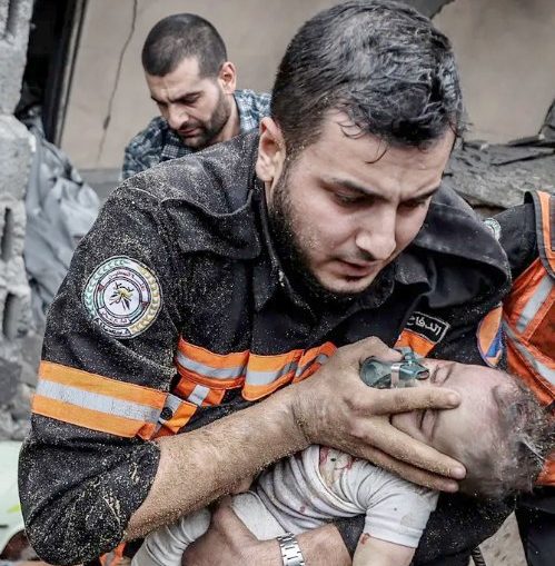 Foto de socorrista tentando salvar criança de escombros de prédio bombardeado por Israel em Gaza. Bombardeios seriam direcionados por programas de computador.
