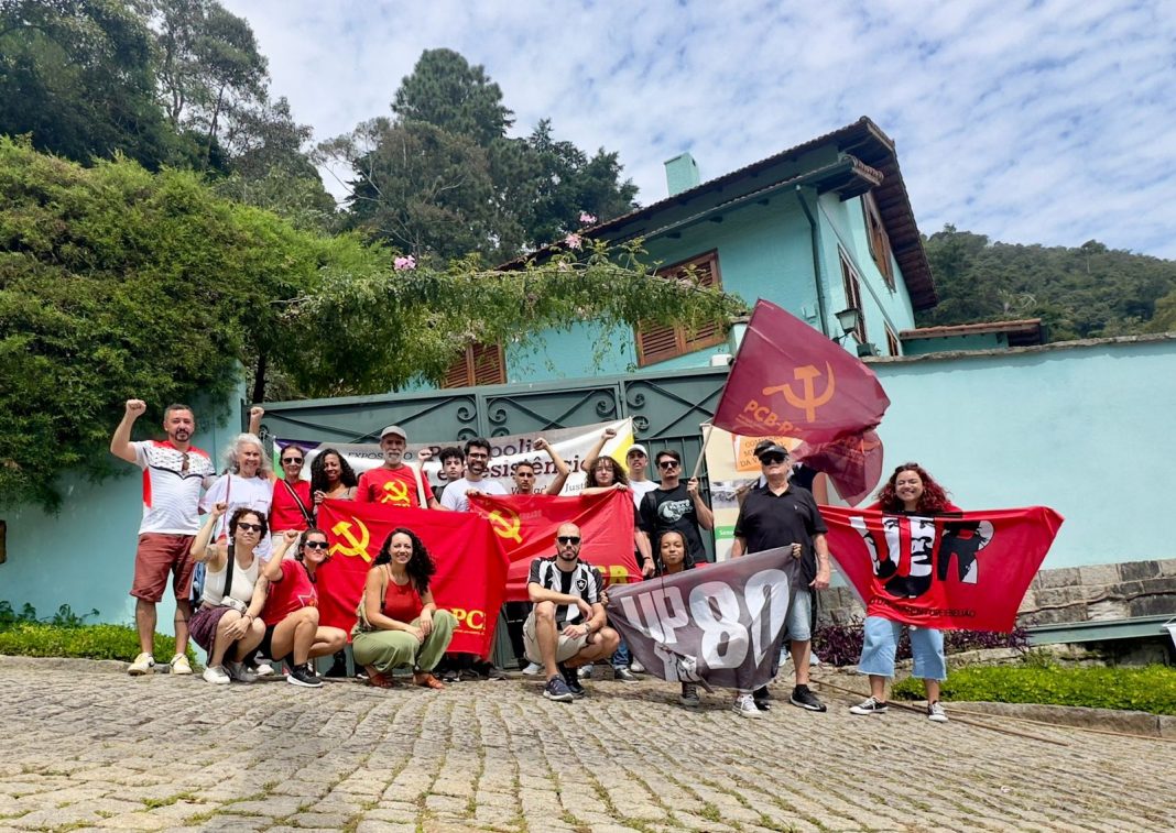 Pessoas com bandeiras em frente a um imóvel de muro azul, onde era a Casa da Morte.