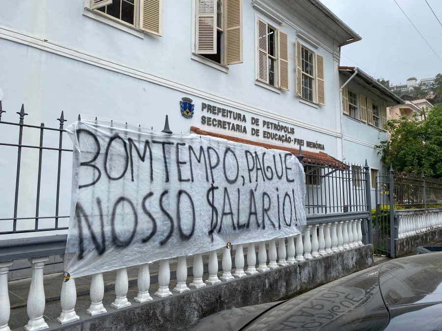 Faixa numa grade em frente ao prédio da Secretaria de Educação de Petrópolis com a frase 