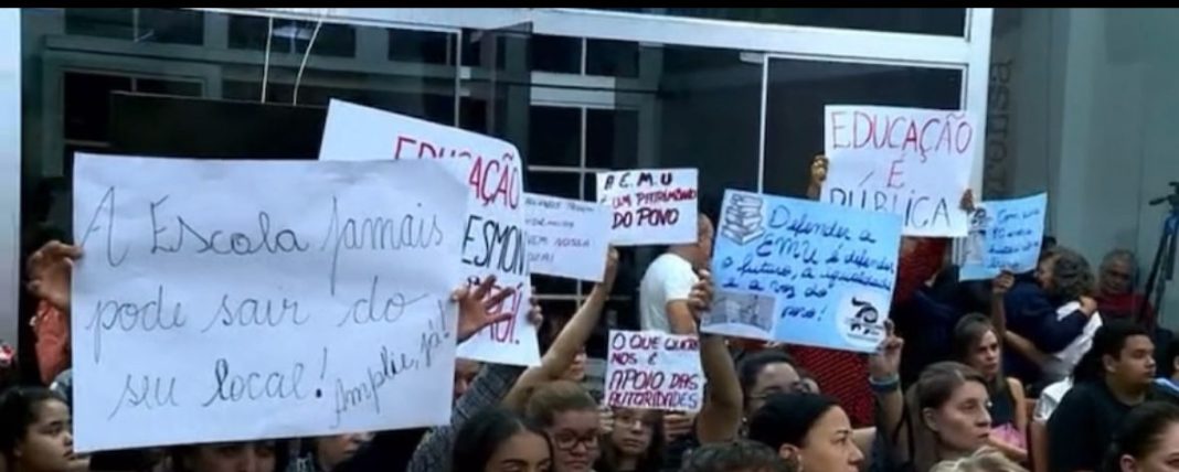 Manifestação da comunidade escolar em Uberaba durante audiência pública, protestando contra o fechamento de uma escola, com cartazes e pessoas reunidas no local.