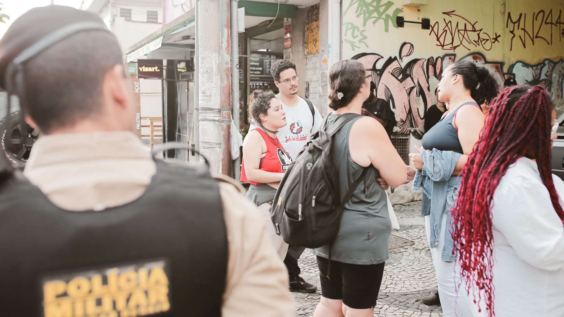 Policial de costas observa militantes conversando com trabalhadoras na calçada.