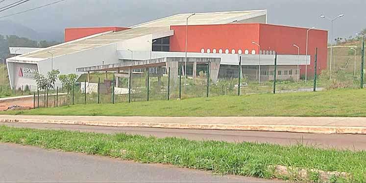 Fachada do prédio do Expominas em São João del-Rei (MG), exibindo uma arquitetura moderna com blocos nas cores branco e vermelho, cercado por uma grade verde e gramado.